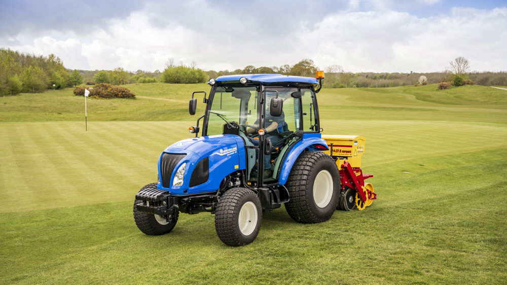 Un Boomer 55 (moteur de 3 cylindres, puissance de 57 ch) avec cabine. Au travail avec un matériel Vredo dédié au sursemis sur les gazons sportifs.