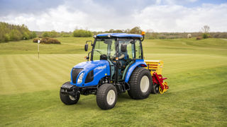 Un Boomer 55 (moteur de 3 cylindres, puissance de 57 ch) avec cabine. Au travail avec un matériel Vredo dédié au sursemis sur les gazons sportifs.